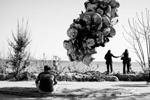 Free Man sitting with balloons overlooking a serene beach scene in black and white. Stock Photo