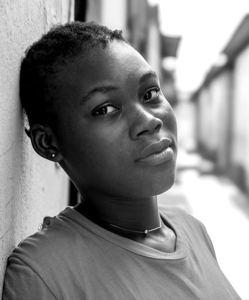 Free Close-up black and white portrait of a young African girl leaning against a wall in an urban alley. Stock Photo