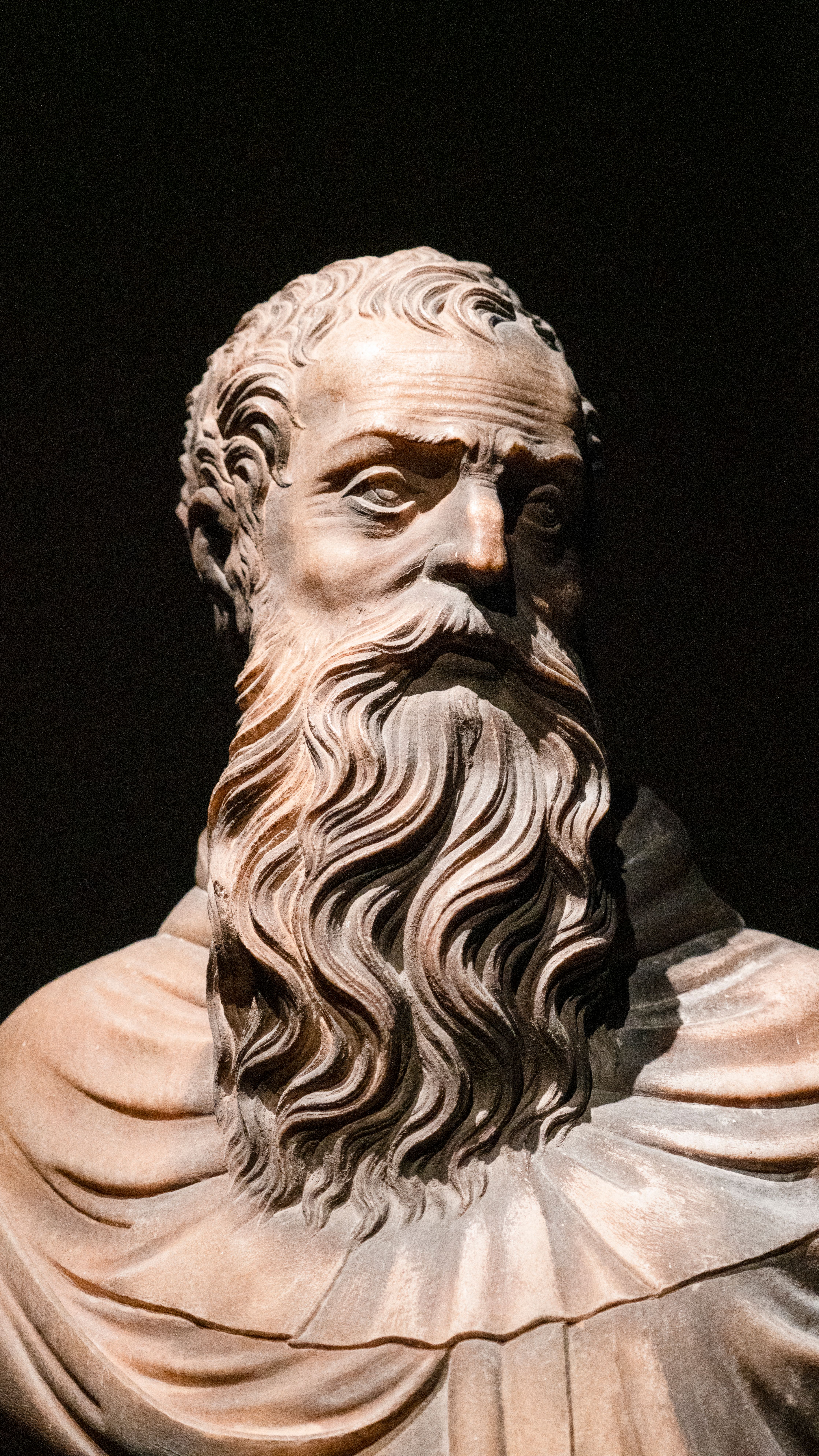A detailed photo of a classical sculpture showcasing a bearded figure against a dark background.
