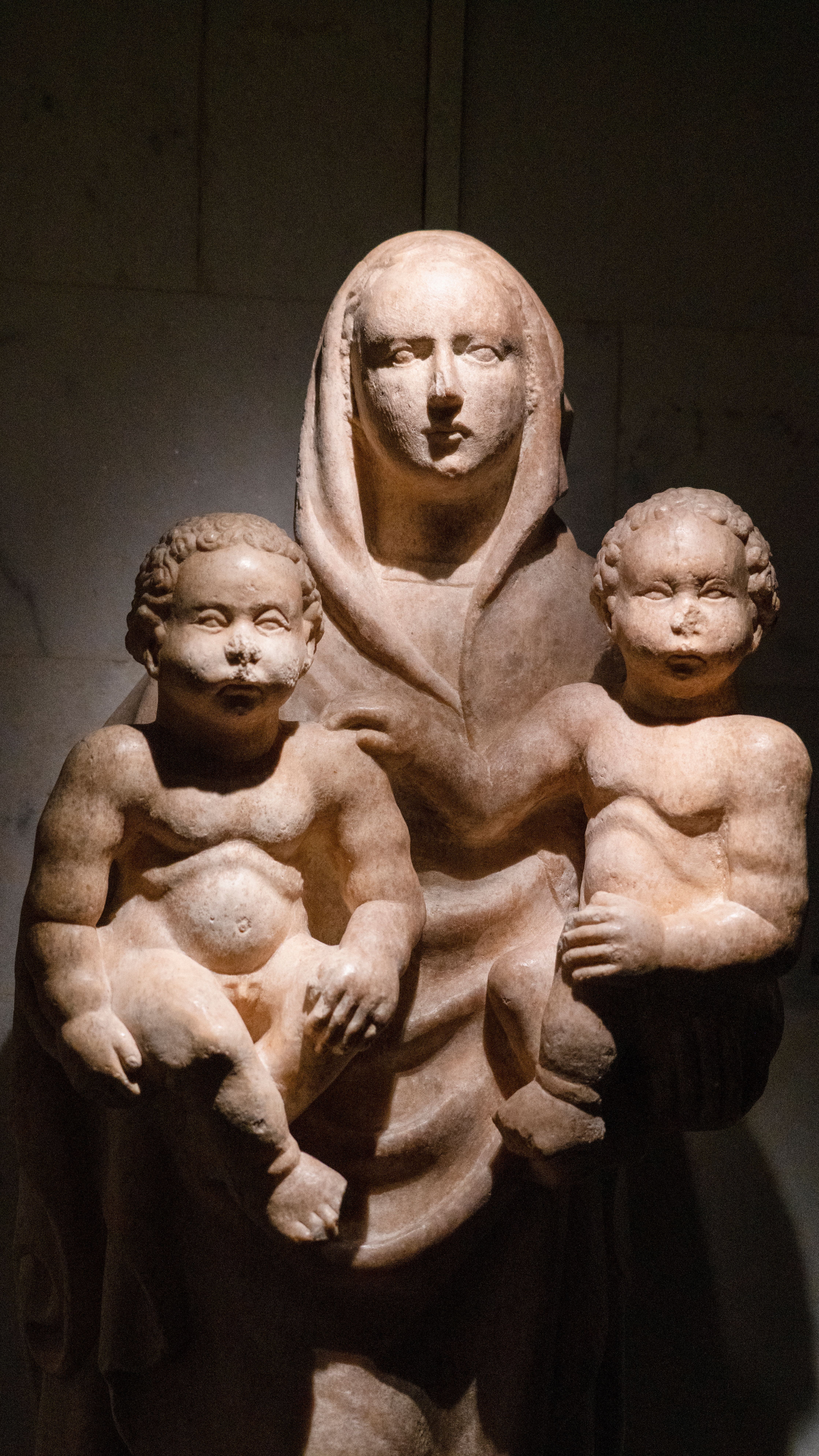 Ancient stone sculpture depicting a mother with two children, symbolizing maternal care.