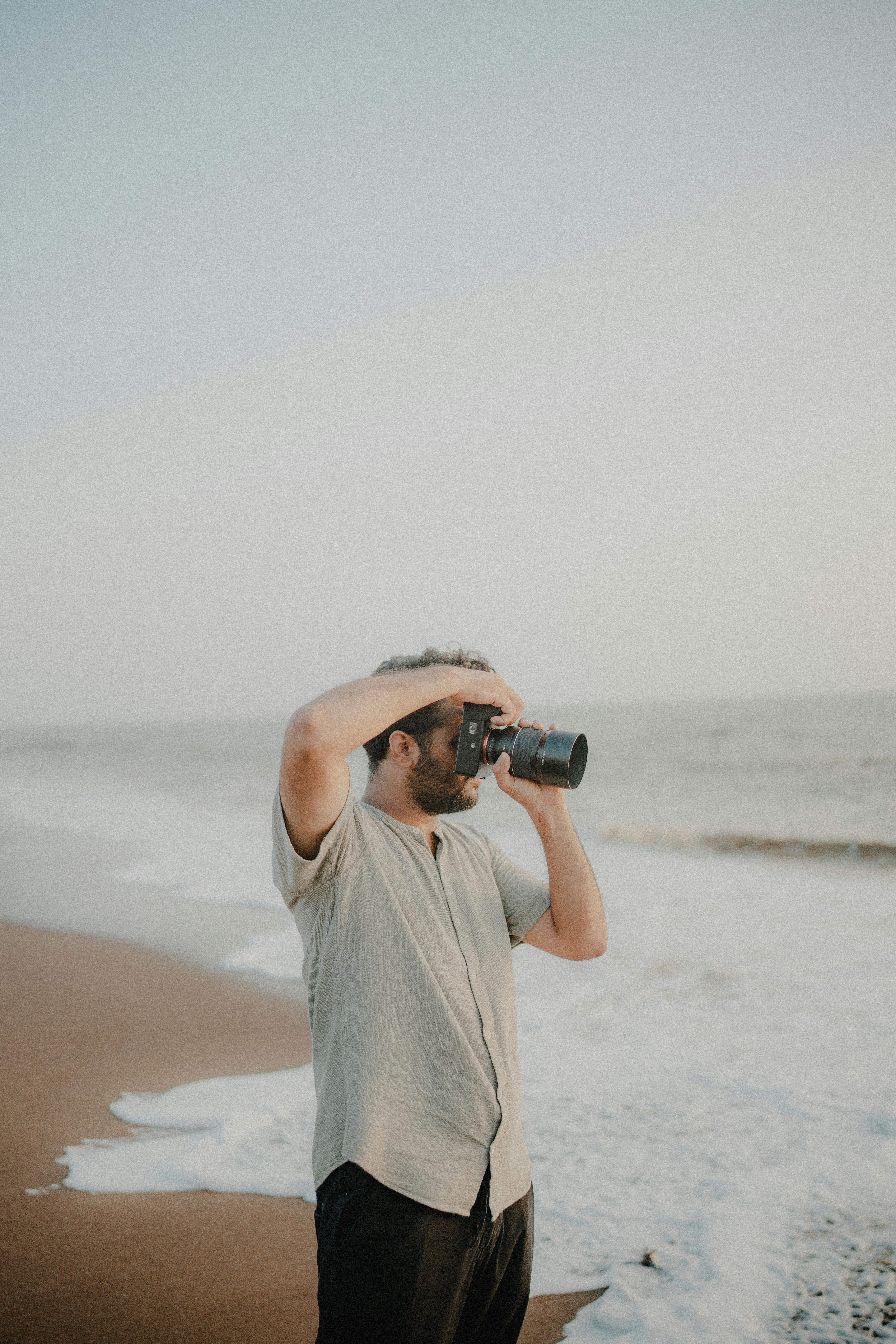 Man using camera to capture ocean waves on a sandy beach at daytime.