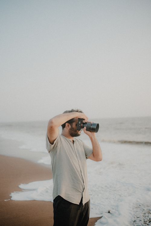 Free Man using camera to capture ocean waves on a sandy beach at daytime. Stock Photo