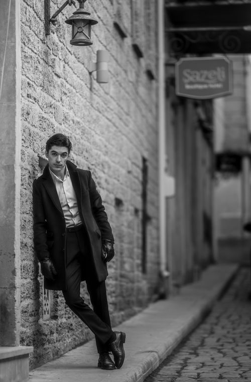 Free Black and white photo of a stylish man in Baku, leaning against a wall in a narrow alleyway. Stock Photo