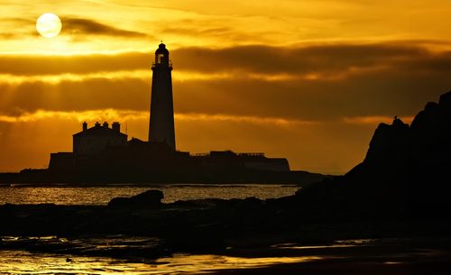 Free St Mary's Lighthouse at sunset with dramatic sky and serene sea reflections in Whitley Bay, UK. Stock Photo