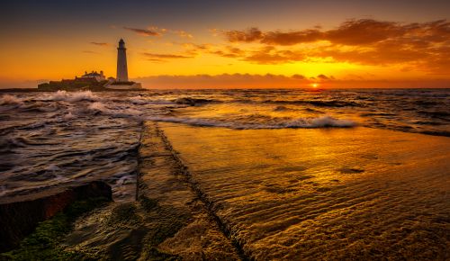 Free A beautiful sunset at St. Mary's Lighthouse in Whitley Bay, UK, with dramatic sky and reflections. Stock Photo