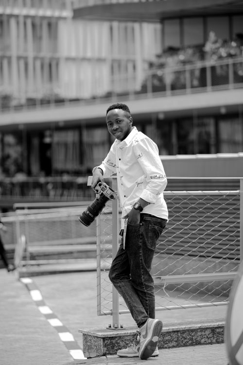 Free Black and white photo of a photographer leaning and smiling in an urban setting. Stock Photo