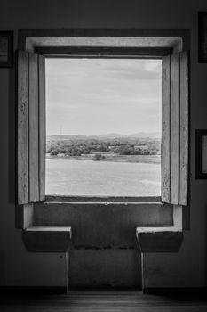 Black and white landscape view from an old window overlooking rural countryside.