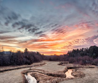 Breathtaking sunset at Misha Mokwa, WI showcasing vibrant skies over tranquil fields and woods.