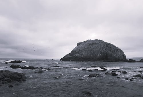 A black and white photo of a rock in the ocean