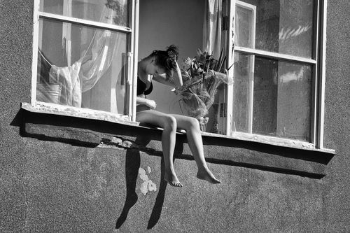 Free A woman sitting in an open window, enjoying sunlight and tranquility. Stock Photo