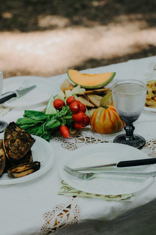 Free A rustic outdoor table setup featuring fresh vegetables, fruits, and tableware. Perfect for a summer picnic. Stock Photo