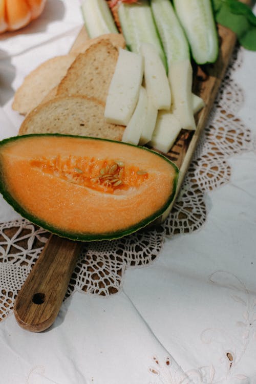 A melon, cucumber, and bread on a wooden cutting board