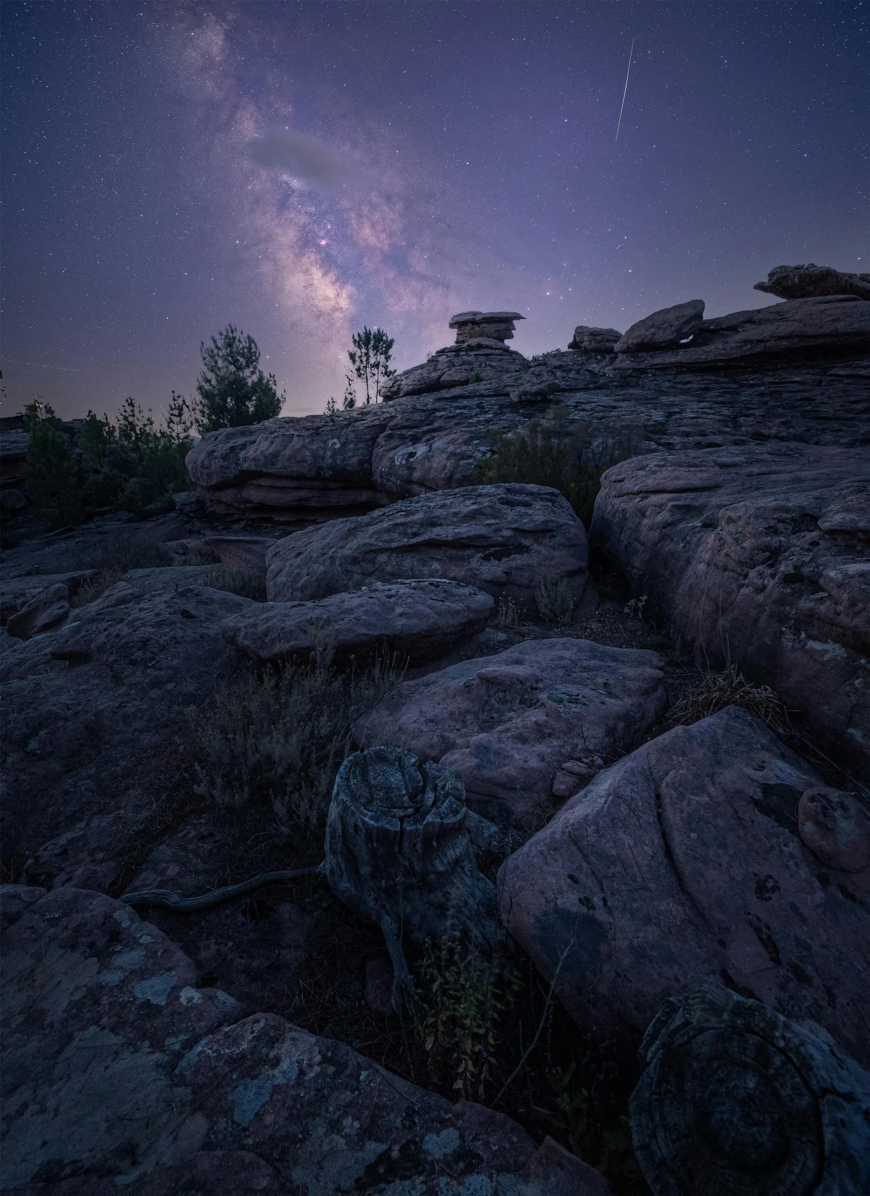 Long exposure of a rocky landscape under a starry sky with the Milky Way visible.