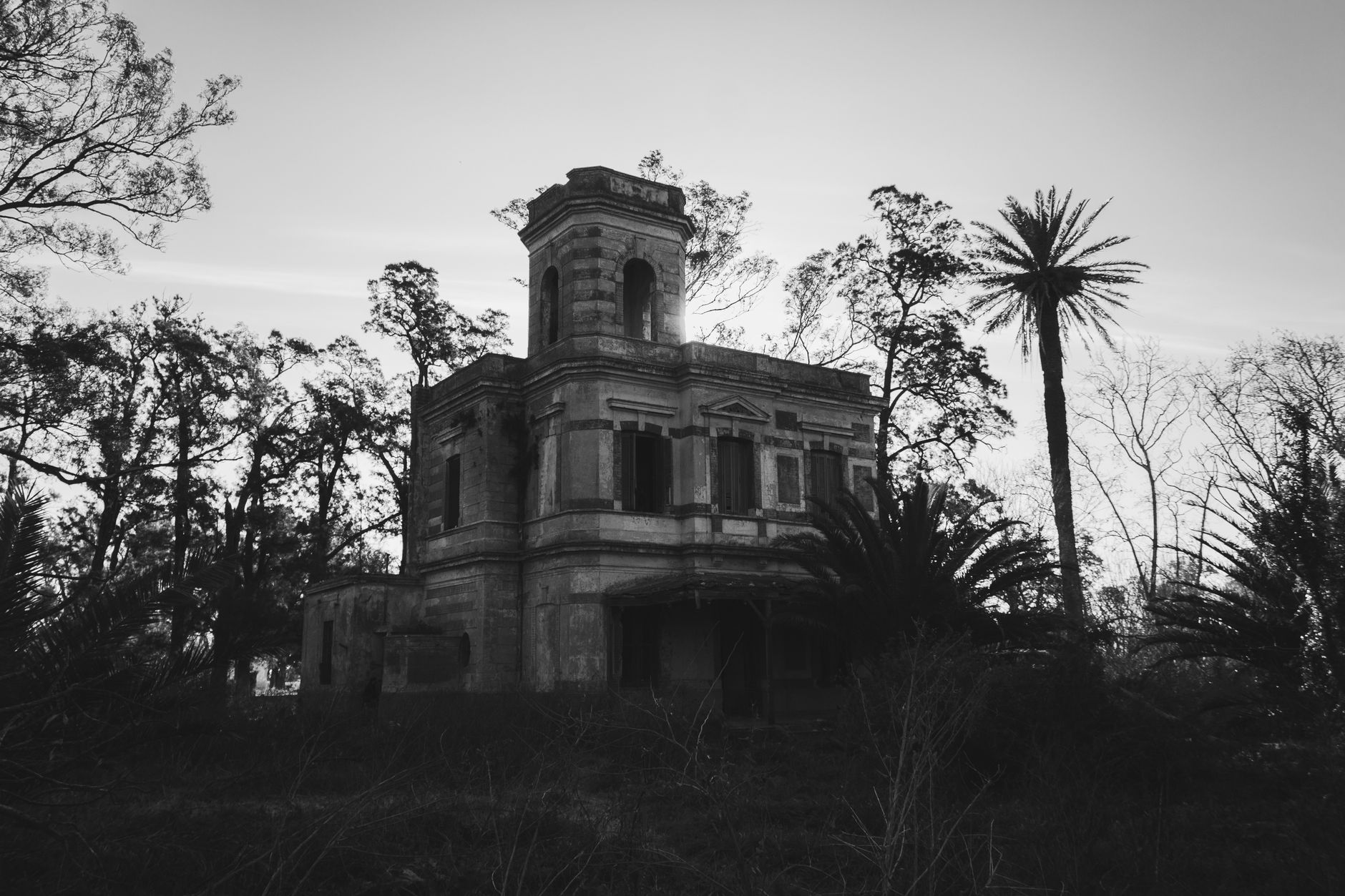 Black and white photo of an abandoned mansion surrounded by trees in Roldán, Argentina.