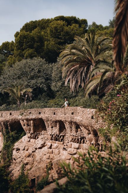 Traveler enjoying a walk along Park Güell's unique stone pathways in Barcelona, surrounded by palm trees.
