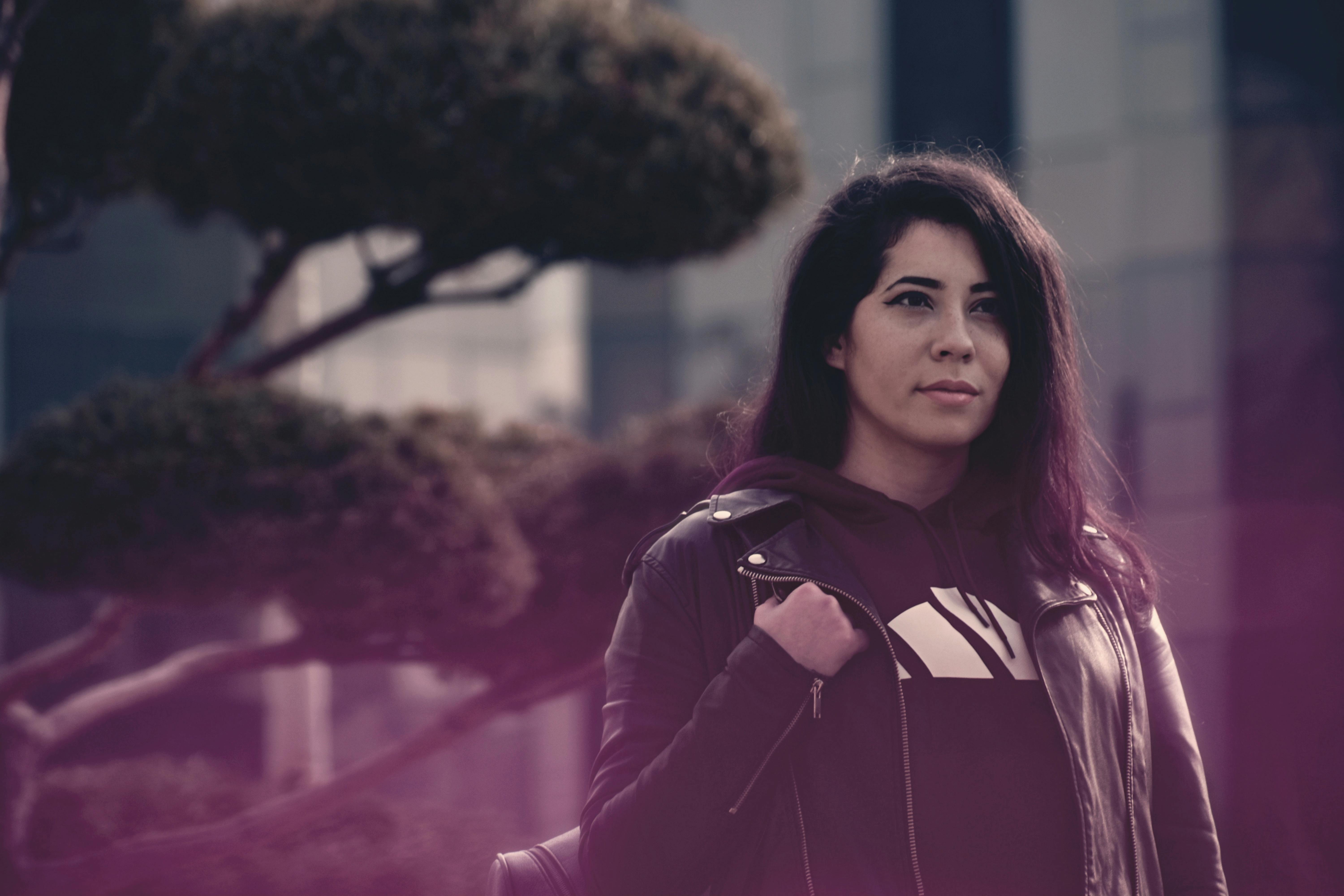 一位时尚女性穿着黑色皮夹克，在现代城市建筑中若有所思地摆姿势