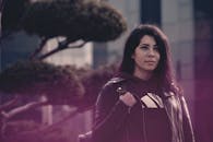 一位时尚女性穿着黑色皮夹克，在现代城市建筑中若有所思地摆姿势