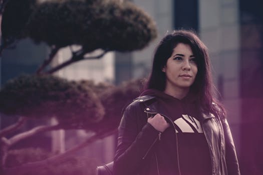 一位时尚女性穿着黑色皮夹克，在现代城市建筑中若有所思地摆姿势