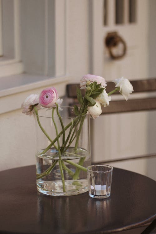 A vase of flowers on a table next to a glass of water