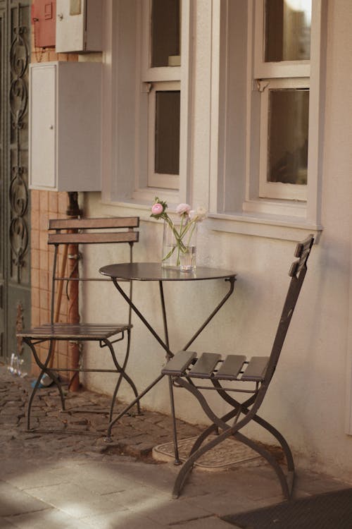 A table and chairs outside a building with a flower vase