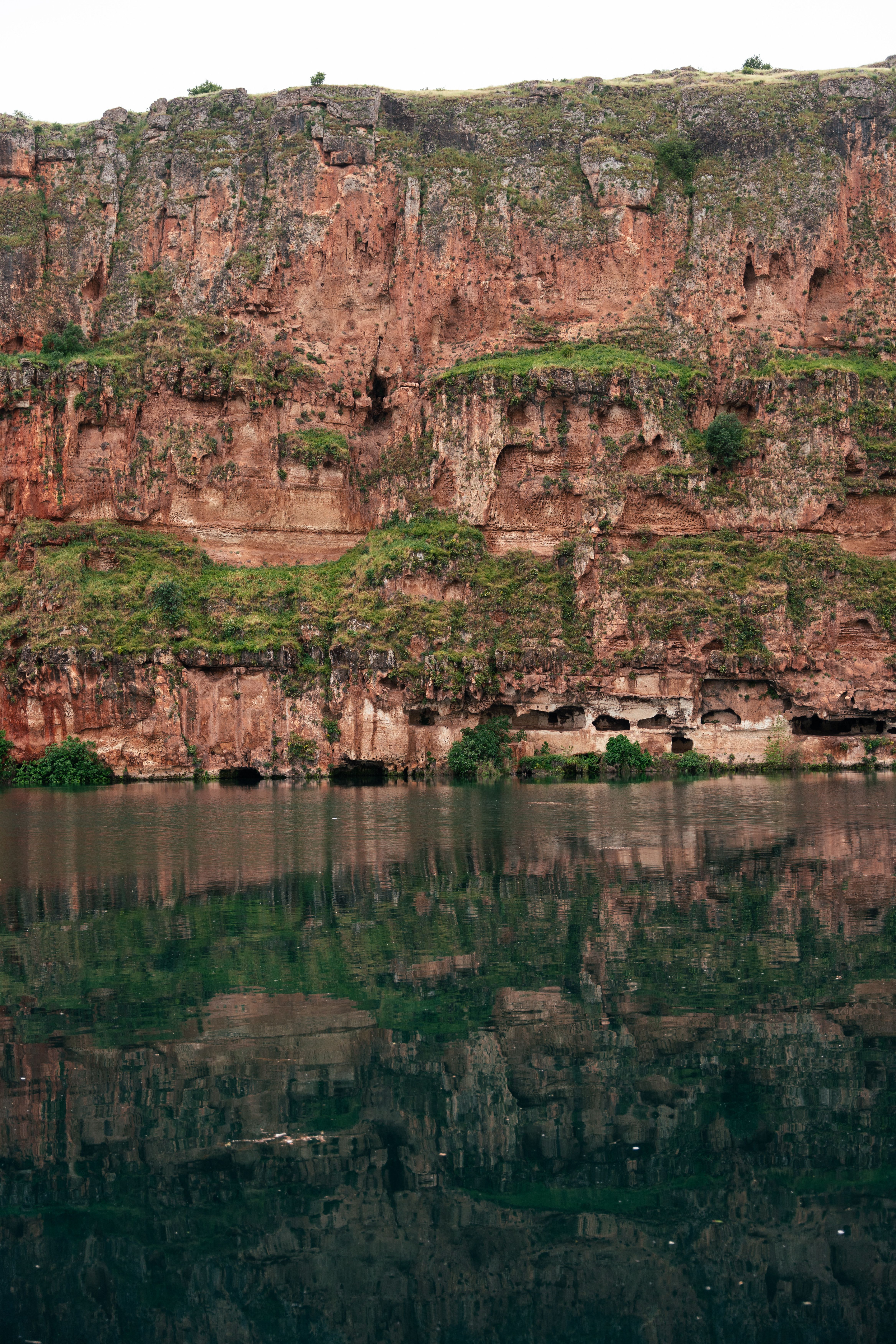 Stunning view of a rugged cliff with vibrant greenery reflected in serene river waters.