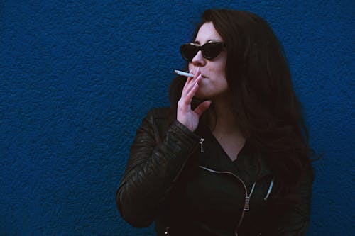 담배를 피우는 파란색 벽에 서있는 여자의 사진