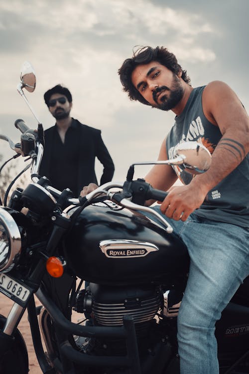 A man on a motorcycle with another man standing next to him