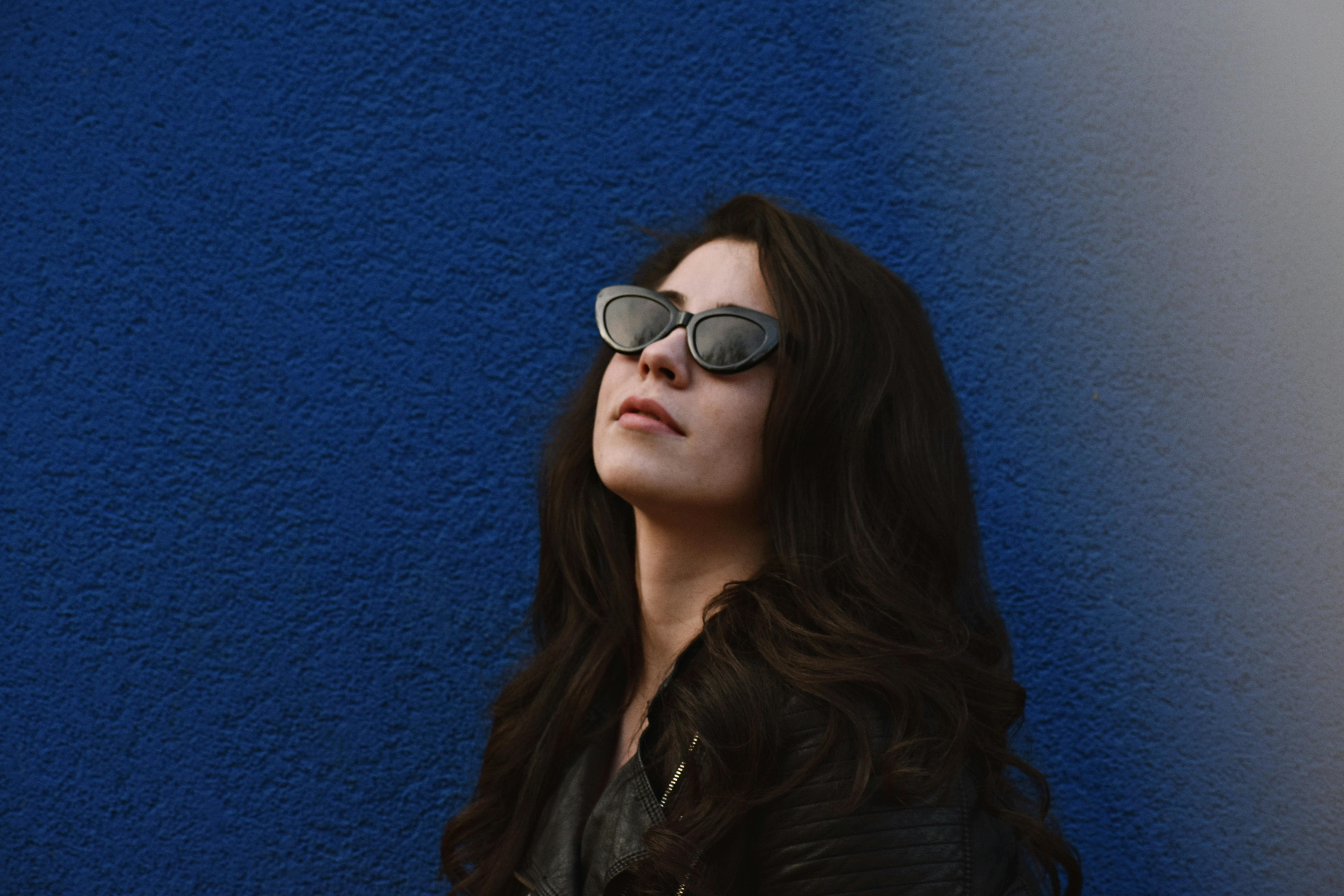 一位时尚的女人穿着黑色皮夹克、戴着太阳镜，在蓝色墙壁前拍摄肖像