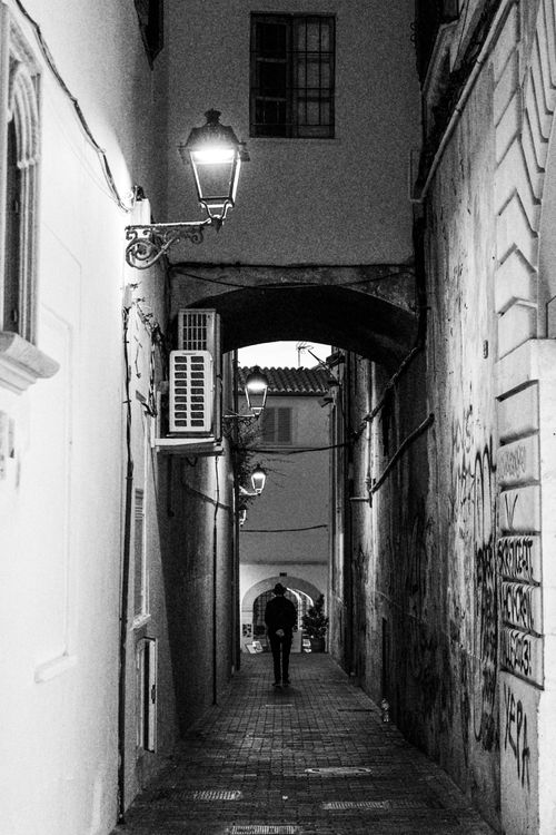 Free A solitary figure walks down a dimly lit urban alley at night, creating a moody atmosphere. Stock Photo