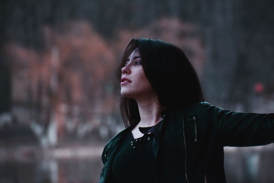 A woman in a black leather jacket looks pensive outdoors during the fall season.