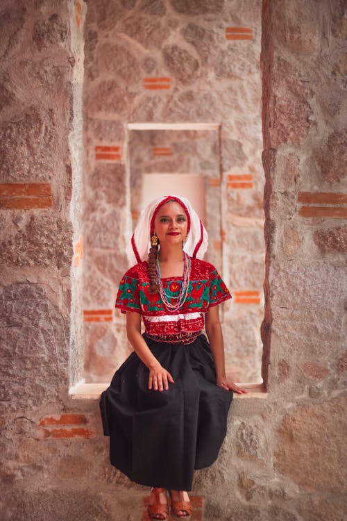 A woman in traditional mexican clothing sitting on a stone wall