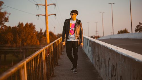 Free A fashionable man in a leather jacket walks on a bridge during sunset, exuding urban style. Stock Photo