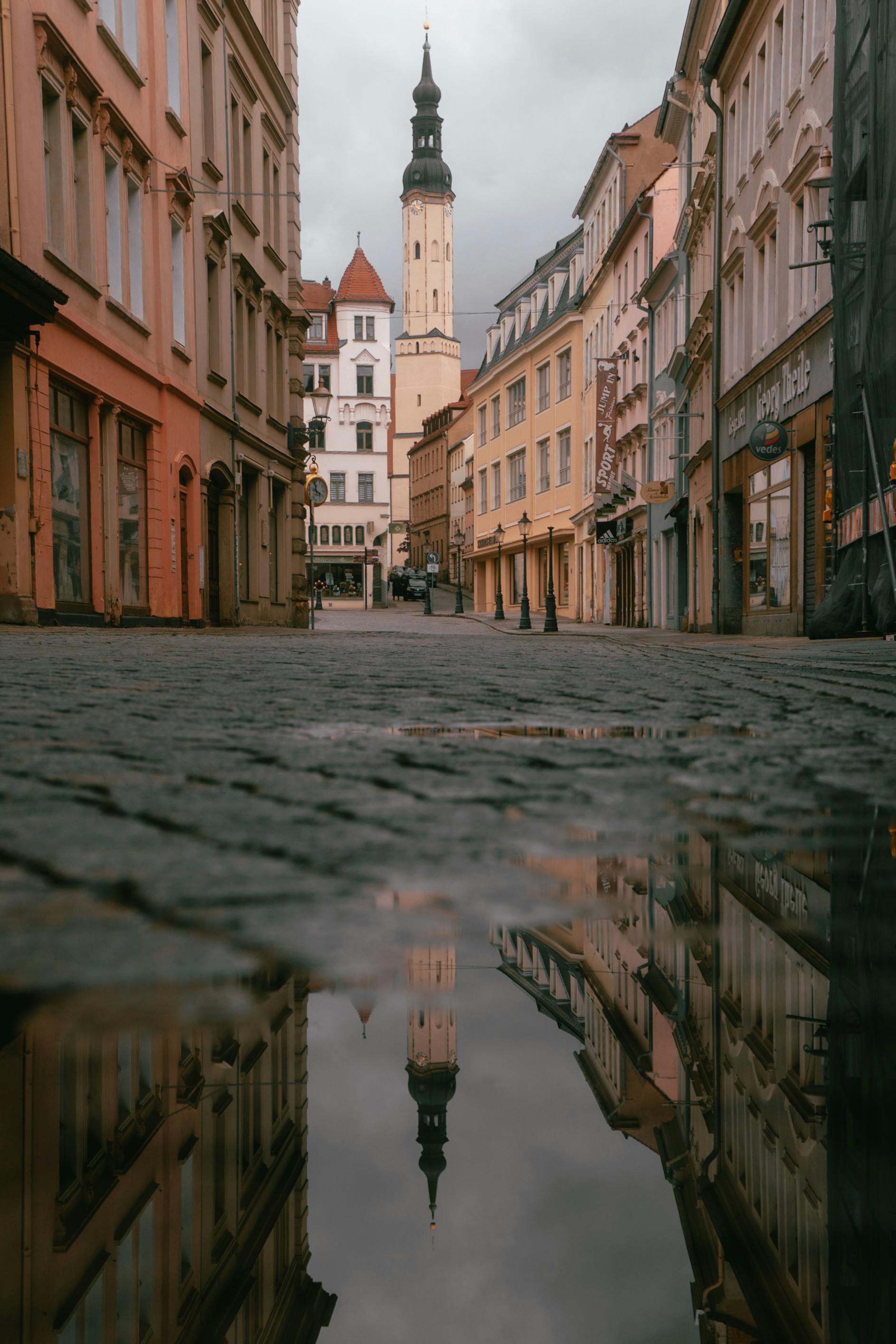Capture of historic street in Zittau with a tower's reflection in a puddle, showcasing beautiful architecture.