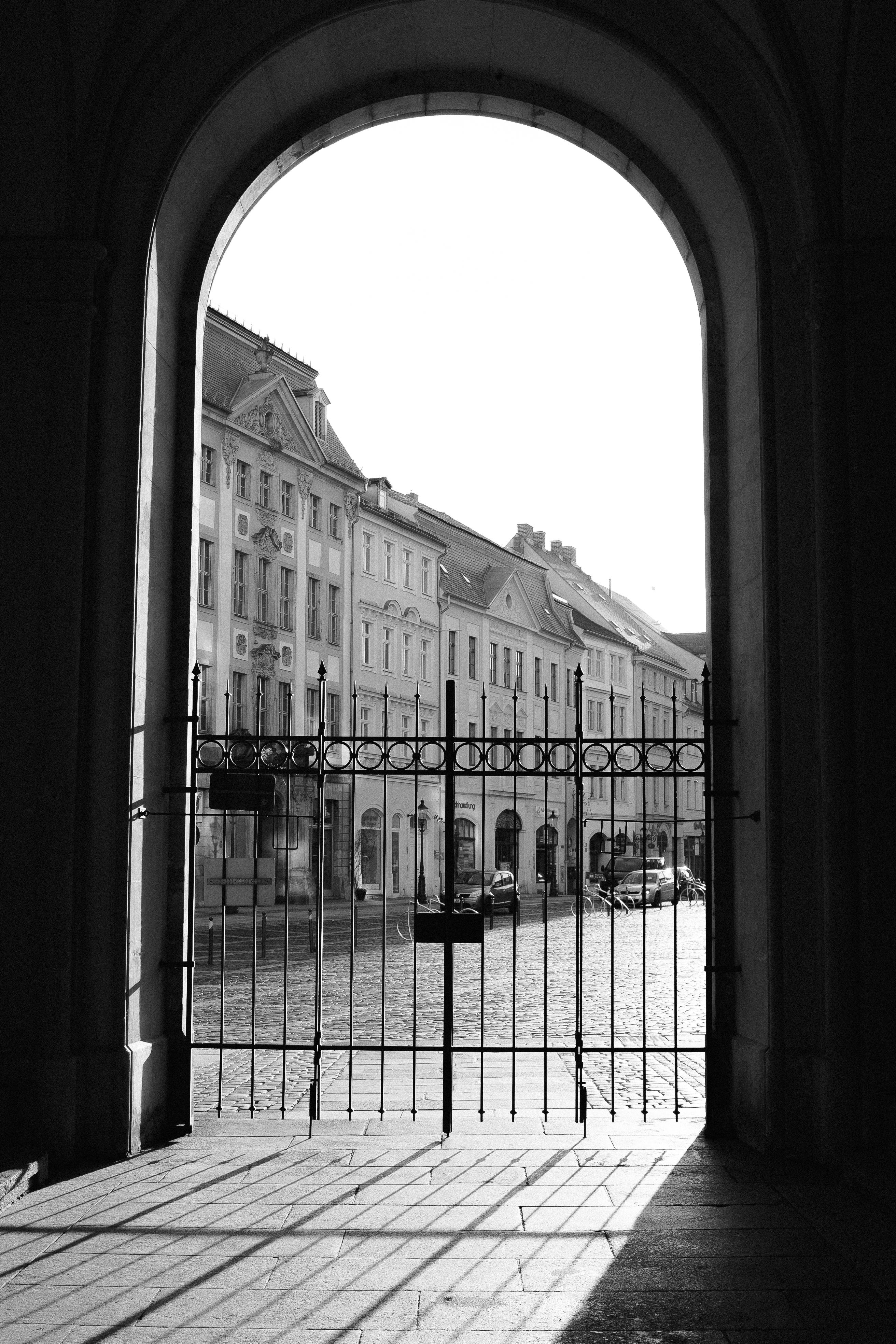 Black and white photo of an urban street through a historic archway in Zittau, highlighting architectural charm.