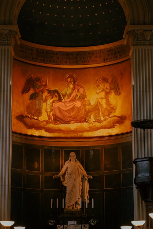 A statue of jesus in a church with a painting on the wall