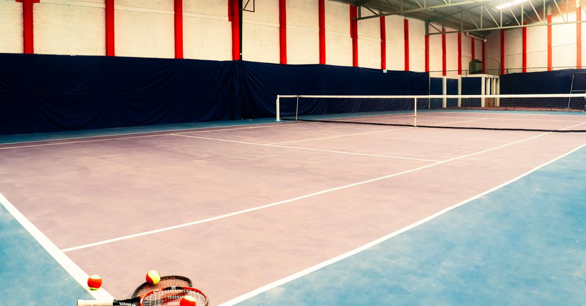 Empty indoor tennis court with rackets and balls in the foreground, showcasing a sports arena setup.