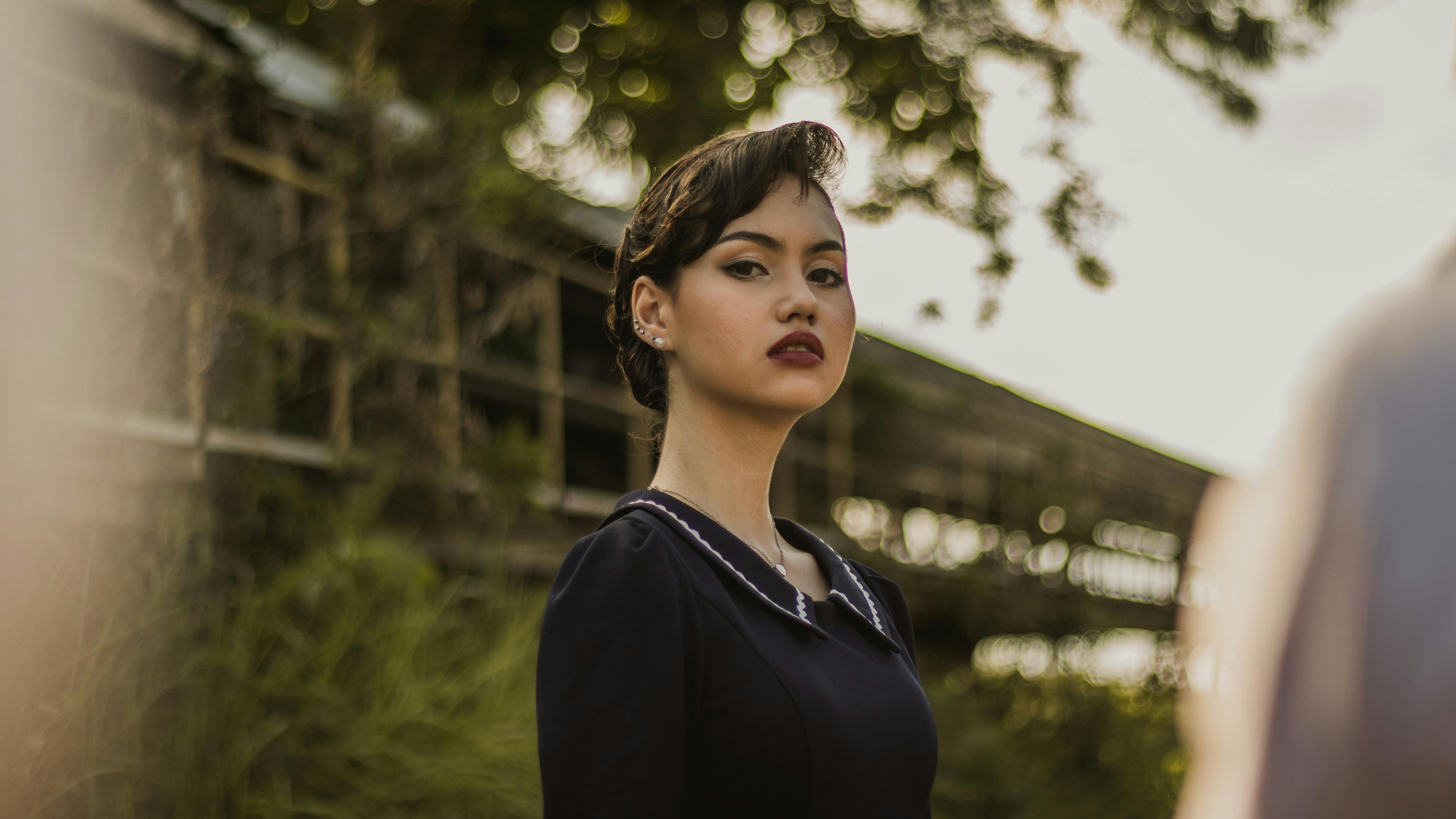 Stylish woman in elegant attire posing outdoors with soft bokeh background.