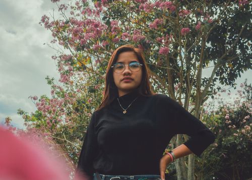 Free Stylish woman posing confidently among blooming pink trees under a cloudy sky. Stock Photo
