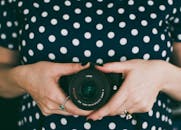 一名女子身穿圆点连衣裙，手拿相机