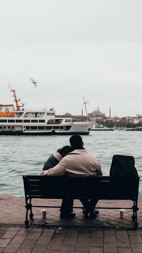 A couple sitting on a bench in front of a boat