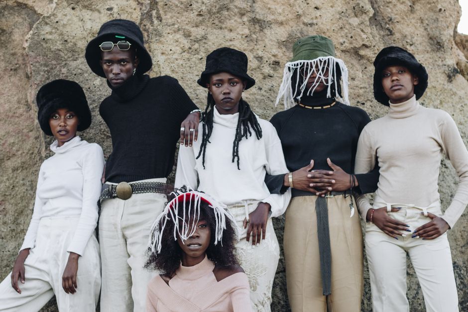 A diverse group of stylishly dressed young people pose against a rocky backdrop.