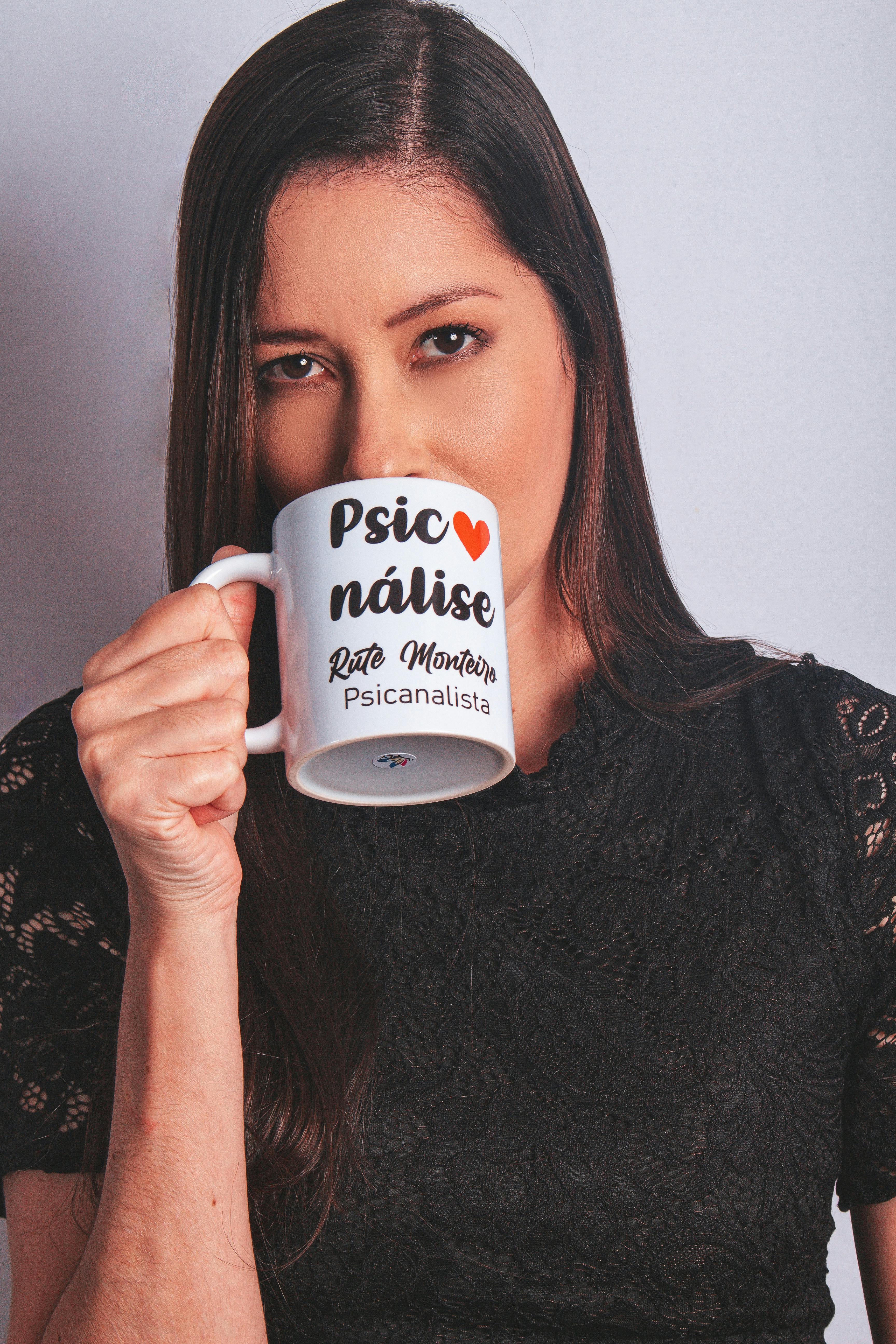 Portrait of a woman holding a mug with Portuguese text against a plain background.