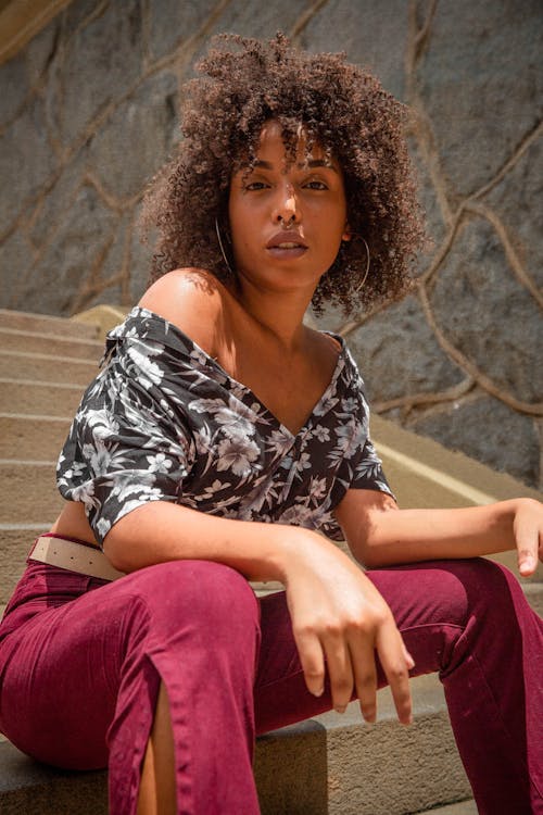 Femme Portant Un Haut à épaules Dénudées à Fleurs Noir Et Blanc Et Un Pantalon Rouge Assis Sur Un Escalier