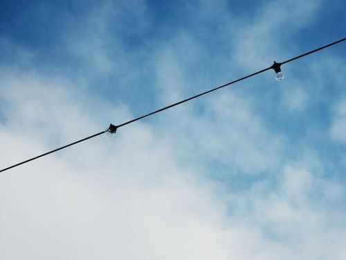 Free Minimalist view of light bulbs on a wire set against a clear blue sky with clouds. Stock Photo
