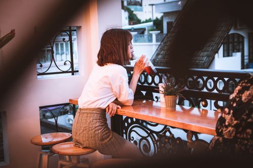 Free A young woman sips a beverage on a stylish balcony at sunset. Stock Photo