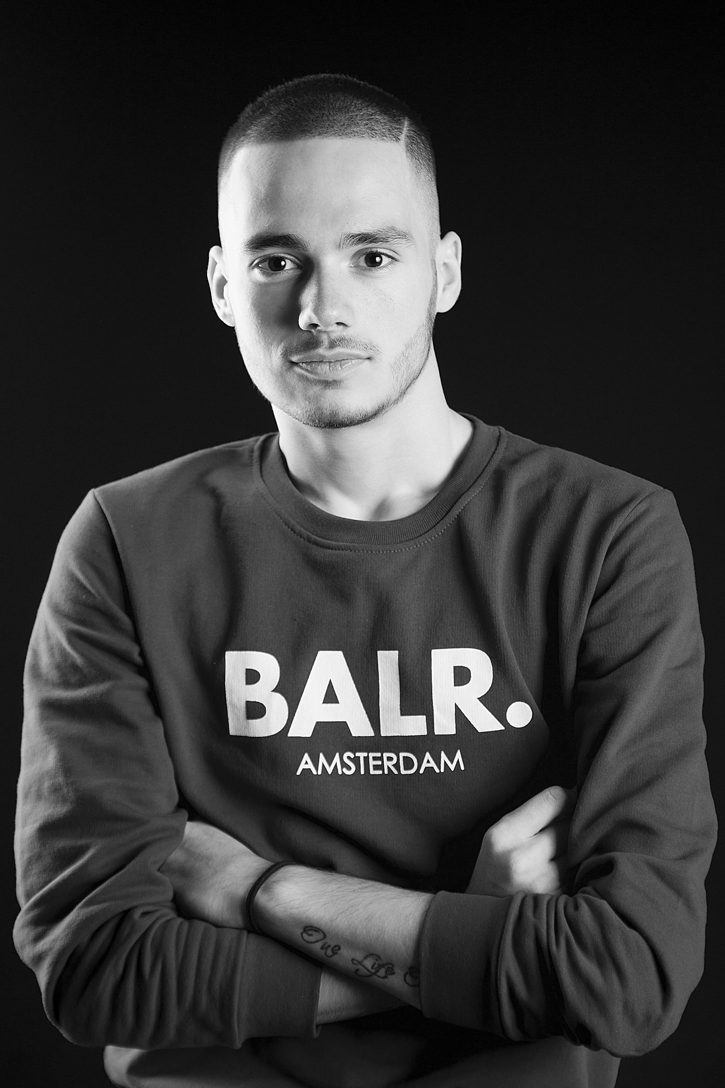 Black and white portrait of a man with folded arms wearing a BALR. sweatshirt.