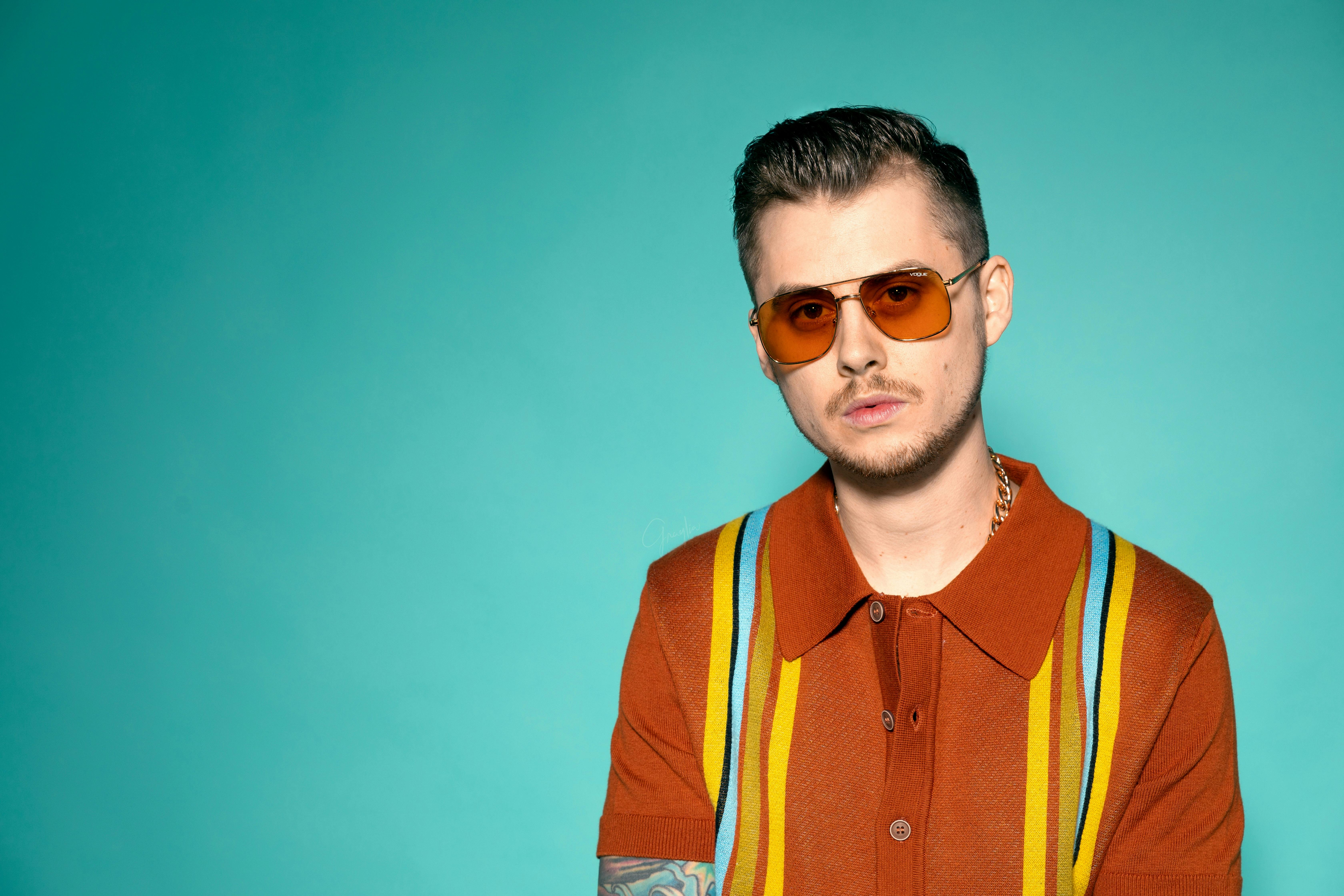 一名男子身着休闲装，戴着太阳镜，在蓝色背景下摆姿势的肖像