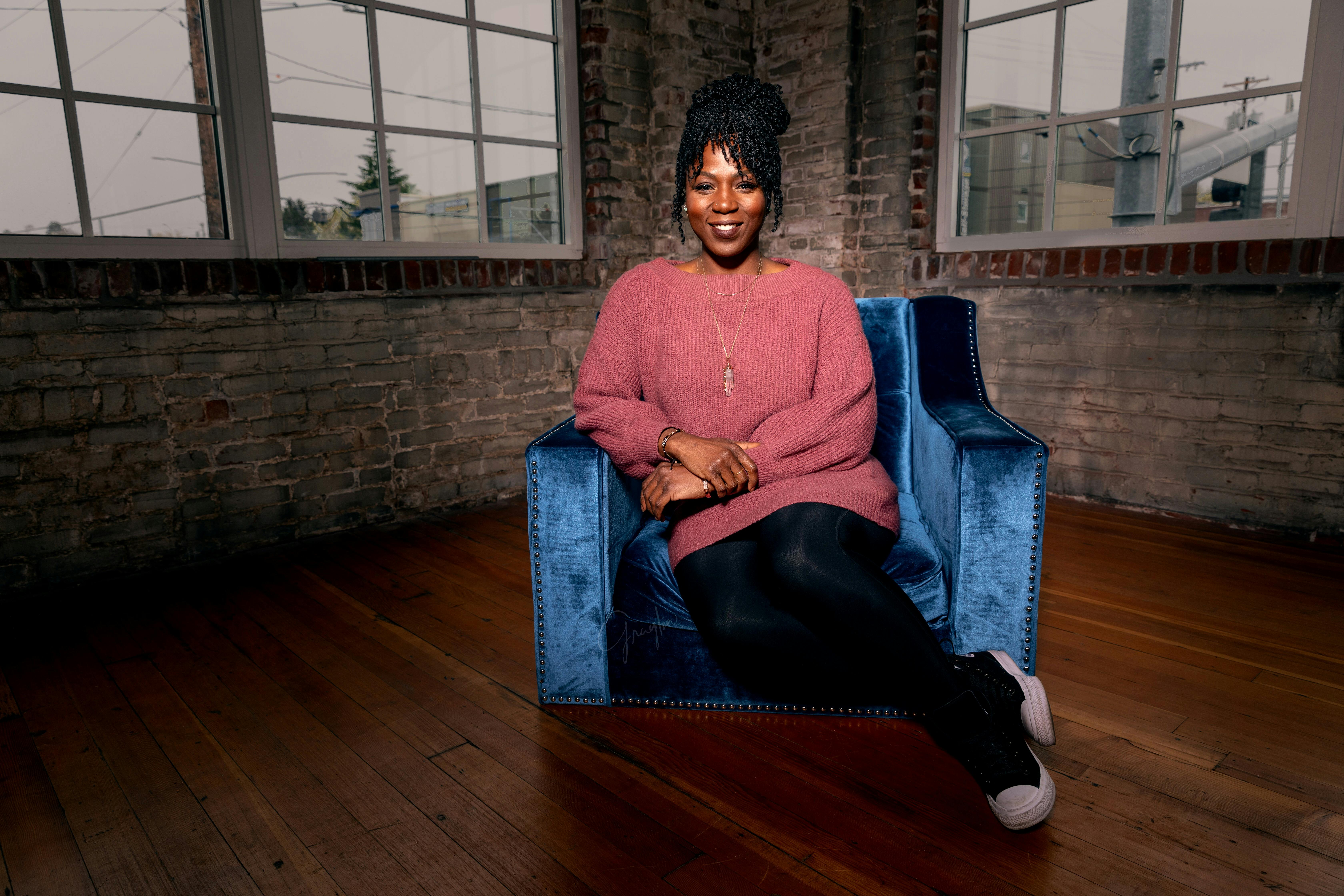 一位穿着舒适毛衣的非洲裔美国妇女坐在别致的扶手椅上，热情地微笑着