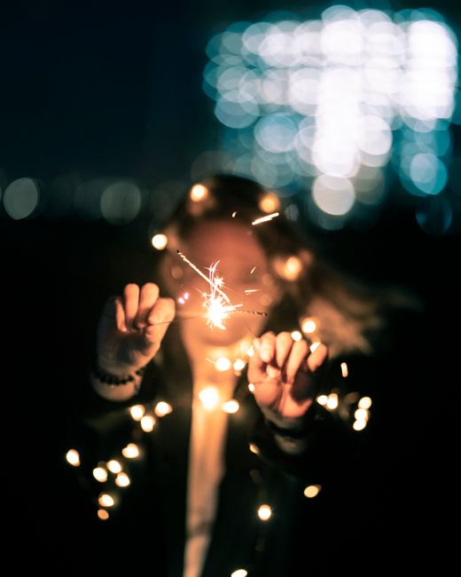 A young woman holding sparklers at night, surrounded by bokeh lights, symbolizing celebration.