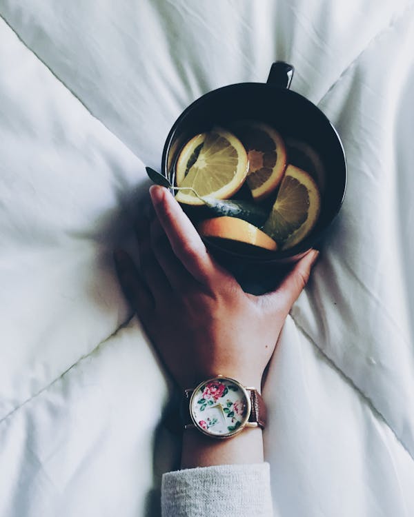 무료 흰색 침대 위안 자 위에 슬라이스 레몬과 함께 블랙 세라믹 머그잔을 들고 여자 스톡 사진